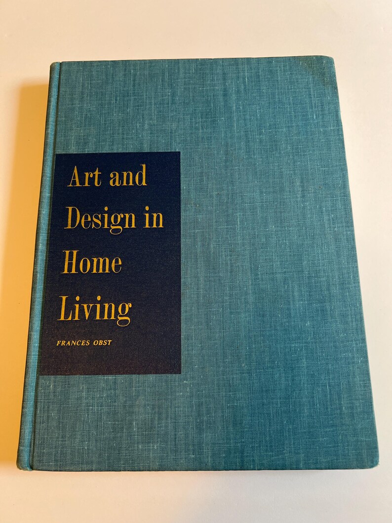 以下が含まれることがあります： 「Art and Design in Home Living」というタイトルが金色で、紺色の長方形のラベルに書かれた、ターコイズ色のハードカバーの本。著者の名前、Frances Obstはタイトルの下に印刷されています。