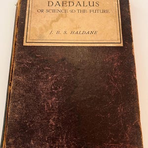 May include: A vintage hardcover book with a dark brown, textured cover and a rectangular tan label on the front. The text on the label reads DAEDALUS OR SCIENCE & THE FUTURE by J. B. S. HALDANE. The edges of the book show signs of wear and age.