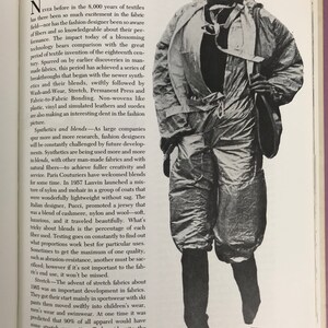 May include: A black and white photograph of a person wearing a silver jumpsuit. The person is standing with their legs slightly apart and their arms at their sides. They are wearing a silver jumpsuit with a zipper down the front and a silver belt. The person is looking at the camera. The text "Silver Jumpsuit 76." is printed in the bottom right corner of the image.