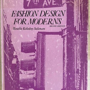 May include: A purple book cover with the title "Fashion Design for Moderns" and the author "Rosalie Kolodny Salomon". The book is a second edition and features a graphic of a city street with a sign that reads "7th Ave."