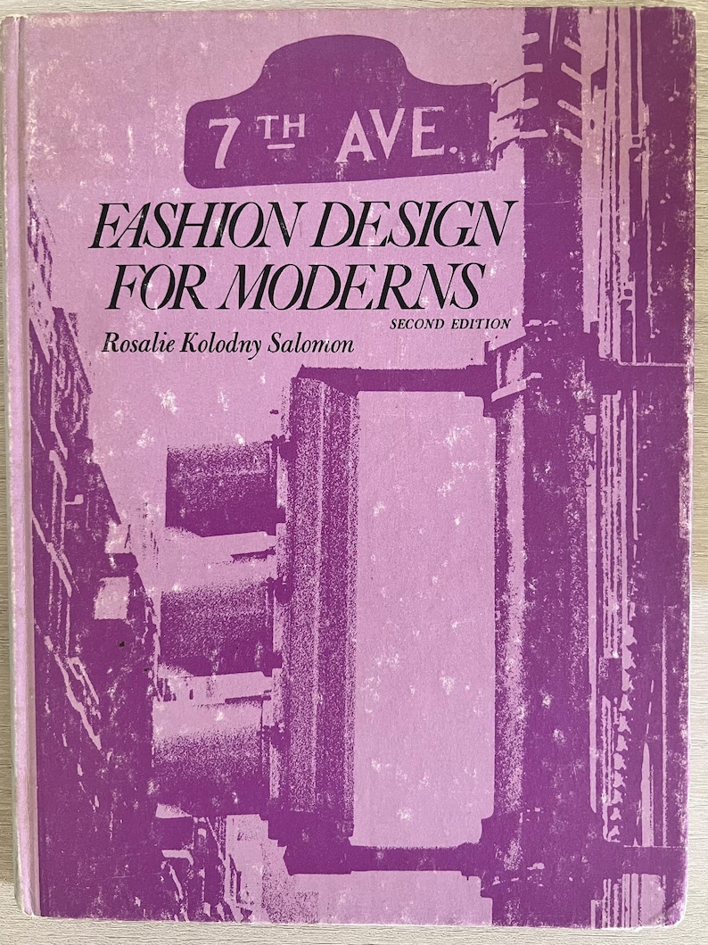 May include: A purple book cover with the title "Fashion Design for Moderns" and the author "Rosalie Kolodny Salomon". The book is a second edition and features a graphic of a city street with a sign that reads "7th Ave."