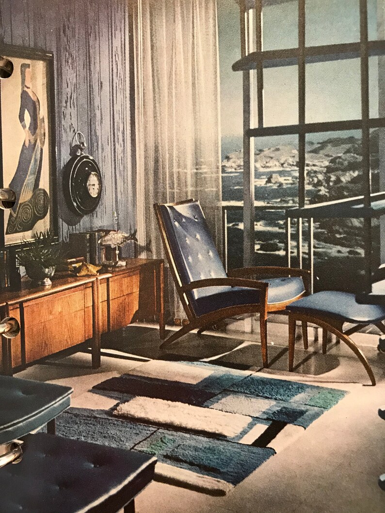 Puede incluir: Una sala de estar de estilo moderno de mediados de siglo con un sill&oacute;n y un reposapi&eacute;s azules, un armario de madera y una alfombra con un patr&oacute;n geom&eacute;trico. La habitaci&oacute;n tiene una gran ventana con vista al oc&eacute;ano.