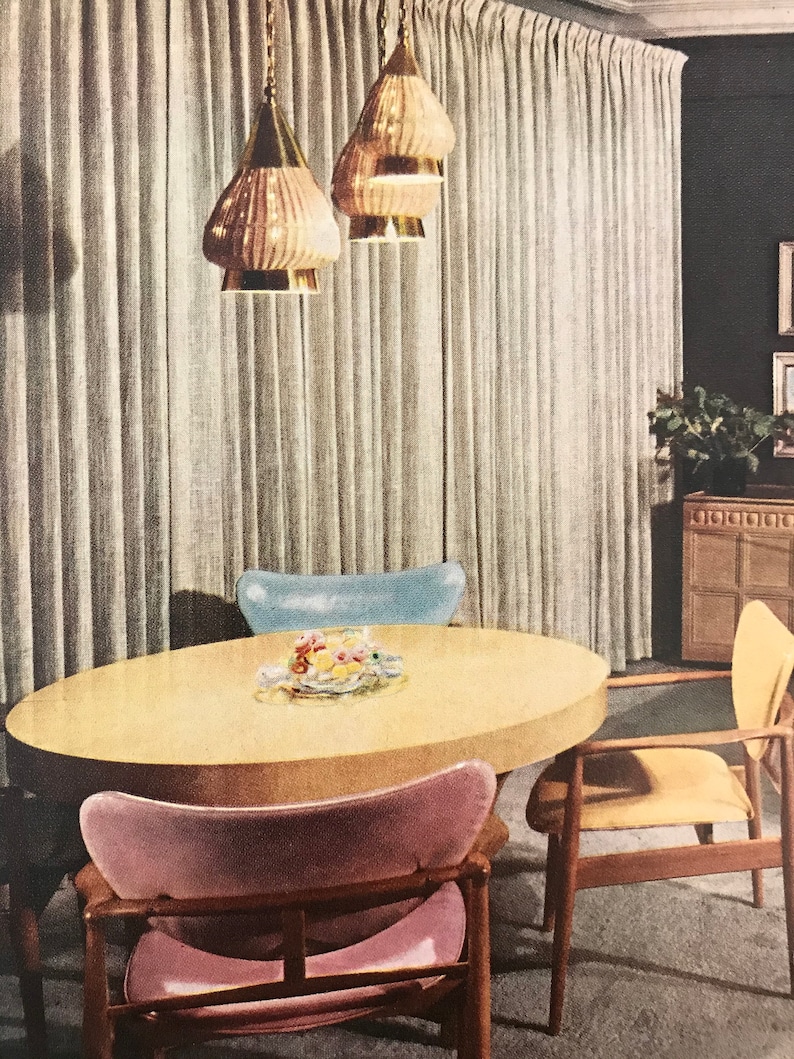 Puede incluir: Un comedor de estilo moderno de mediados de siglo con una mesa redonda de madera clara y cuatro sillas. Las sillas est&aacute;n tapizadas en tela rosa, azul y amarilla. Tres l&aacute;mparas colgantes doradas cuelgan del techo sobre la mesa.