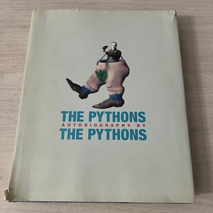 Könnte beinhalten: Ein Buch mit dem Titel The Pythons Autobiography by The Pythons mit hellgrauem Einband. Das Cover zeigt eine surreale Illustration des Oberkörpers einer Person, die aus einem Paar großer Beine mit braunen Schuhen und blauen Socken ragt.