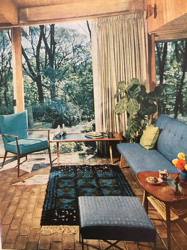 Puede incluir: Una sala de estar con un sof&aacute; azul, un sill&oacute;n azul, una mesa de caf&eacute;, un reposapi&eacute;s azul y una mesa auxiliar de madera. La habitaci&oacute;n tiene una ventana grande con cortinas y vista a los &aacute;rboles. Hay una alfombra en el suelo con un patr&oacute;n azul y negro.