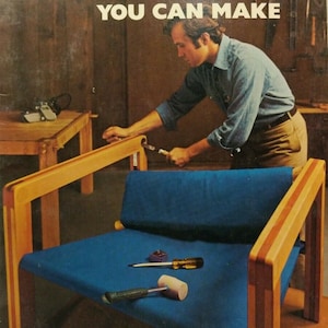 May include: A book titled "Furniture You Can Make" with a photo of a man assembling a wooden chair with a blue fabric seat. The chair is on a wooden floor and there are tools on the seat.