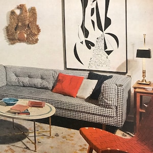 Puede incluir: Un interior de sala de estar con una pintura abstracta en blanco y negro colgada en la pared sobre un sof&aacute; a cuadros gris y blanco. El sof&aacute; tiene almohadas rojas y blancas. Una mesa de caf&eacute; redonda con una tapa de m&aacute;rmol se encuentra frente al sof&aacute;. Una silla roja tejida se encuentra en primer plano.