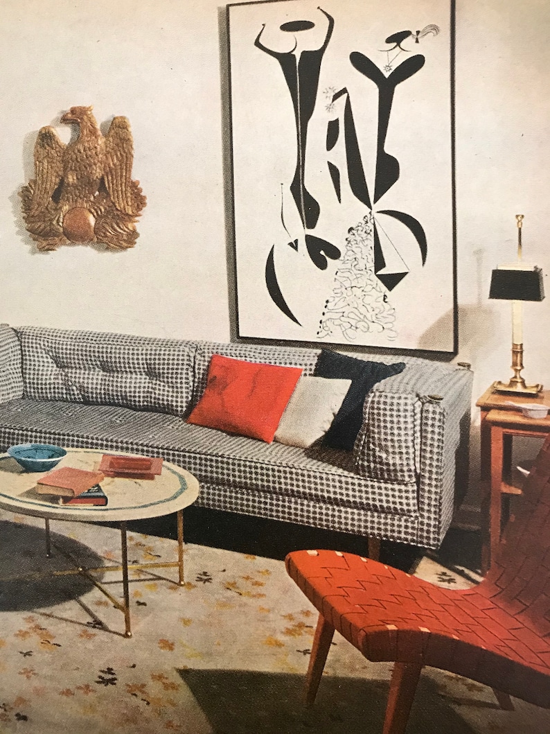 Puede incluir: Un interior de sala de estar con una pintura abstracta en blanco y negro colgada en la pared sobre un sof&aacute; a cuadros gris y blanco. El sof&aacute; tiene almohadas rojas y blancas. Una mesa de caf&eacute; redonda con una tapa de m&aacute;rmol se encuentra frente al sof&aacute;. Una silla roja tejida se encuentra en primer plano.