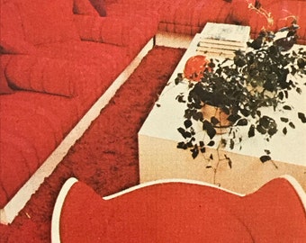 May include: A large red sectional sofa with matching cushions, a white rectangular coffee table with a potted plant, and a curved red and white chair. The furniture is arranged on a deep red shag carpet in a room with a white wall and artwork.