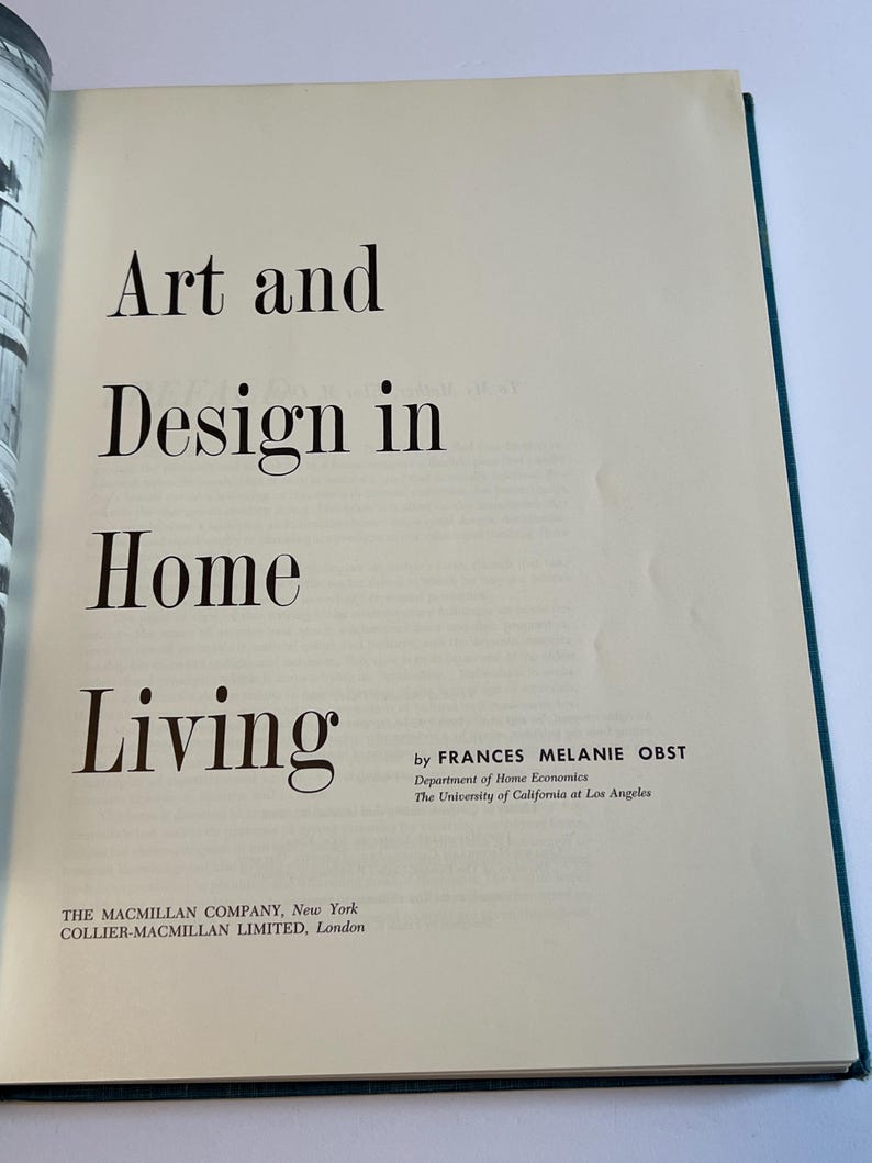 以下が含まれることがあります： 「Art and Design in Home Living」というタイトルが大きな黒い文字で書かれた開かれた本。著者であるフランシス・メラニー・オストの名前と出版社の情報も表示されています。ページはオフホワイトで、緑色の縁取りがあります。