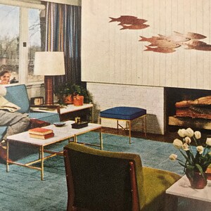 Puede incluir: Una sala de estar de estilo moderno de mediados de siglo con un sof&aacute; azul, una mesa de caf&eacute;, un otomano azul, una chimenea y un jarr&oacute;n de tulipanes blancos. La habitaci&oacute;n est&aacute; decorada con una escultura de pared de peces.