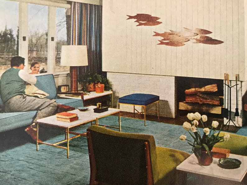 Puede incluir: Una sala de estar de estilo moderno de mediados de siglo con un sof&aacute; azul, una mesa de caf&eacute;, un otomano azul, una chimenea y un jarr&oacute;n de tulipanes blancos. La habitaci&oacute;n est&aacute; decorada con una escultura de pared de peces.
