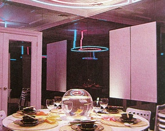 May include: A retro dining room with a round table set for a meal. The table is surrounded by metal chairs and topped with place settings. A large fishbowl sits in the center. Overhead, neon lights in pink and blue illuminate the room.