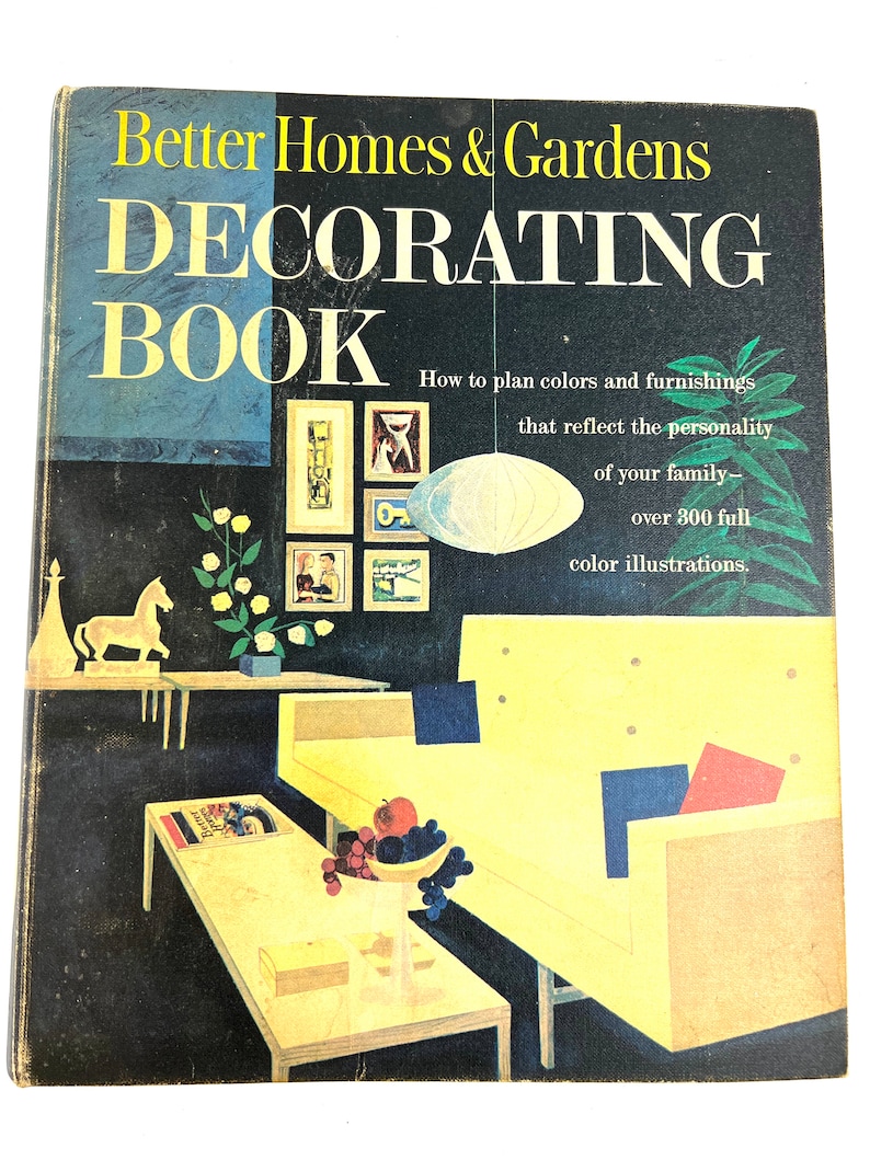 Puede incluir: Un libro vintage titulado "Better Homes & Gardens Decorating Book" con un sof&aacute; amarillo, una mesa de caf&eacute; y un taz&oacute;n de fruta en el fondo. La portada del libro presenta una ilustraci&oacute;n en blanco y negro de un interior de sala de estar.