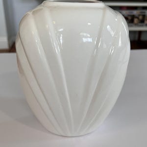 May include: A white ceramic mug with a black handle and the text "But First, Coffee" in a bold, black font. The mug is set against a blurred background, suggesting a cozy setting.