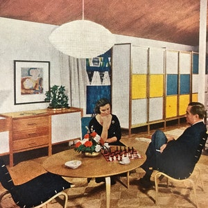Puede incluir: Un sal&oacute;n de estilo moderno de mediados de siglo con una pareja jugando al ajedrez en una mesa redonda de madera. La sala cuenta con un divisor de ambientes con estampado blanco y amarillo, un armario de madera con cajones y una chimenea de ladrillo.