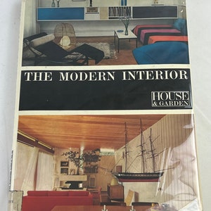 May include: A book titled "The Modern Interior" by House & Garden featuring two interior design photos. The first photo shows a living room with a black chaise lounge, a wicker lampshade, and a blue and white rug. The second photo shows a living room with a wooden ceiling, a white fireplace, and a model ship hanging on the wall.