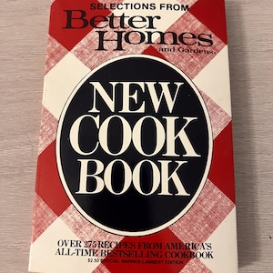 Op de afbeelding: Een kookboek getiteld Selections from Better Homes and Gardens New Cook Book met een rood-wit geblokt patroon op de achtergrond. De kaft bevat een grote zwarte ovaal met witte tekst en de ondertitel Over 275 Recipes from America's All-Time Bestselling Cookbook.