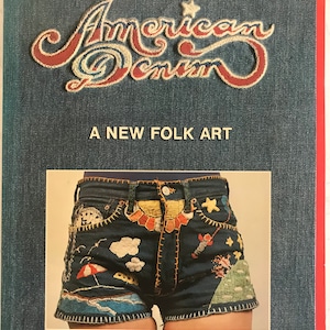 Puede incluir: Una portada de libro con fondo de mezclilla azul. El título "American Denim: A New Folk Art" está bordado en hilo rojo, blanco y azul. La portada también presenta una foto de pantalones cortos de mezclilla decorados con bordados coloridos.