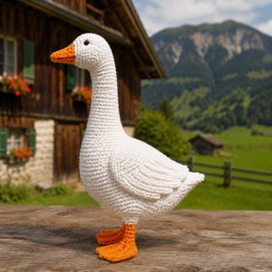 May include: A handcrafted crochet goose toy featuring a white yarn body, a bright orange beak, and matching orange webbed feet. The goose is depicted in a standing position with a textured stitch pattern throughout its entire form.