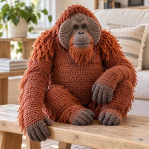 May include: A handcrafted crochet orangutan plush toy featuring a textured, shaggy coat of burnt orange yarn. The figure has a distinct, rounded brown face with dark eyes, a flat nose, and brown hands and feet. It sits in a seated position.