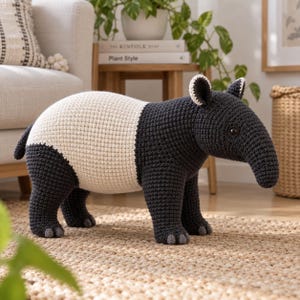 Könnte beinhalten: Eine handgefertigte Häkelfigur eines Tapirs mit dunkel anthrazitfarbenem Kopf, Beinen und Schwanz, kontrastiert durch ein breites, cremefarbenes Band um die Körpermitte. Das Tier hat eine lange, abgerundete Schnauze, kleine dunkle Augen und weiß umrandete Ohren.