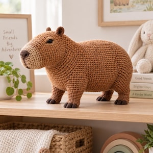 May include: A brown capybara stuffed animal made of crocheted yarn. The figure features a textured, rounded body, small dark ears, a blunt snout with a dark brown nose, and four short legs with dark brown feet. The eyes are small and black.