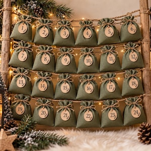 Può includere: Un calendario dell'avvento con ventiquattro sacchetti in tessuto verde oliva appesi a una scala di legno. Ogni sacchetto è chiuso con uno spago e decorato con un'etichetta rotonda in legno numerata da uno a ventiquattro con inchiostro nero.