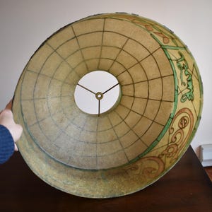 May include: A large, vintage lampshade with a globe design. The shade is beige with a grid pattern and decorative elements in green and brown. The lampshade has a circular opening in the center.