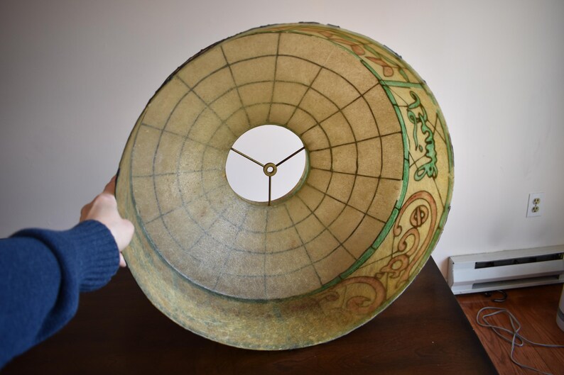 May include: A large, vintage lampshade with a globe design. The shade is beige with a grid pattern and decorative elements in green and brown. The lampshade has a circular opening in the center.