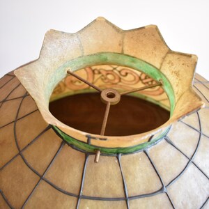 May include: A dome-shaped lamp shade featuring a grid of dark metal lines over translucent beige panels. The top opening has a scalloped edge with a green band and a metal spider fitter with three spokes centered around a central ring.