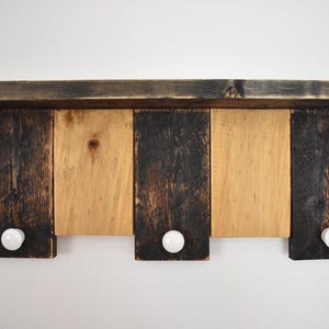 May include: A rustic wooden shelf with three hooks, each with a white ceramic knob. The shelf is stained in a dark brown color with natural wood accents.