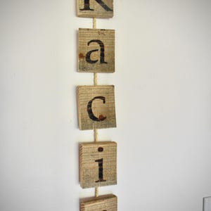 May include: A vertical wall hanging consisting of five square wooden blocks strung together on a light-colored rope. Each block features a single dark, burned-in letter, spelling out the name Kacie from top to bottom in a mix of cases.