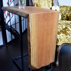May include: A live edge side table with a natural wood top and a black metal frame. The table has a unique, organic shape and measures approximately 30 inches long.