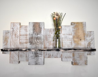 May include: A rustic wooden shelf with a distressed white finish. The shelf is made of reclaimed wood and has a black painted edge. A small vase with dried flowers sits on the shelf.
