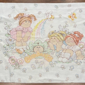 May include: White Cabbage Patch Kids sheet with illustrations of the dolls, a rainbow, a bunny, and a butterfly. The sheet has a repeating floral pattern and the text "Cabbage Patch Kids".