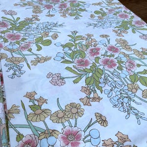 Peut inclure: Tissu blanc avec un motif floral composé de fleurs roses, brunes et bleues. Les fleurs sont disposées en grappes et entourées de feuilles vertes.