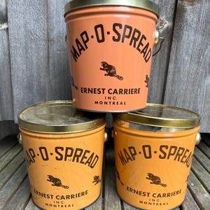 May include: Three orange metal containers with gold lids and a black beaver logo. The containers are labelled "Map-O-Spread Ernest Carriere Inc. Montreal."
