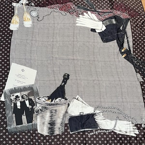 May include: A square scarf featuring a central grey and black glen plaid pattern with a dark brown border. Illustrations include two champagne flutes, a pocket watch, white gloves, a black clutch, a pearl necklace, and a framed photograph of two people.