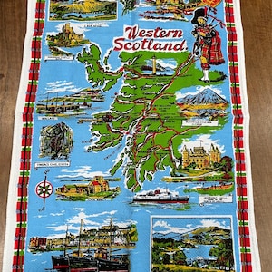 May include: A white cotton tea towel with a map of Western Scotland, featuring illustrations of landmarks and a bagpiper. The text "Western Scotland" is displayed. The border is red and green.