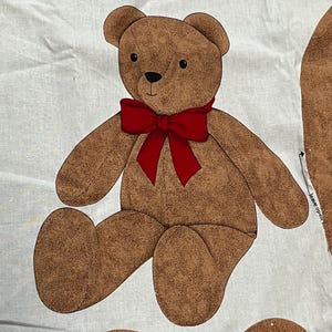 May include: A brown teddy bear illustration with a red bow tie is printed on white fabric. The text "THE V.I.P. BEAR" is printed in red above the bear. Additional bear parts are visible below the bear.