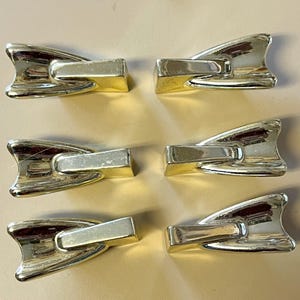 May include: Six gold-toned cabinet door pulls shaped like a pair of flippers. The pulls have a smooth, shiny finish.
