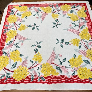May include: A square white tablecloth featuring a border of red wavy lines and a floral pattern of bright yellow mimosa blossoms, green leaves, and delicate pinkish-red fern-like foliage arranged in a decorative frame around the centre.