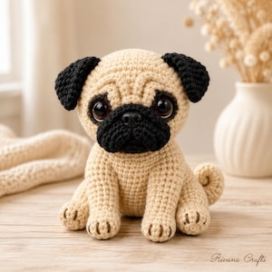May include: A crochet pug toy featuring a tan body, black ears, and a black muzzle. The stuffed animal has large dark brown eyes and a small black nose. The text Rivana Crafts is visible in the bottom right corner of the image.