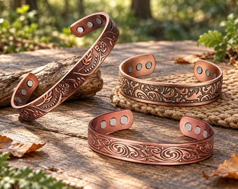 Può includere: Tre bracciali aperti color rame con intricati motivi floreali e a spirale in rilievo. Ogni bracciale presenta piccoli inserti magnetici circolari color argento visibili sulla superficie interna della fascia.
