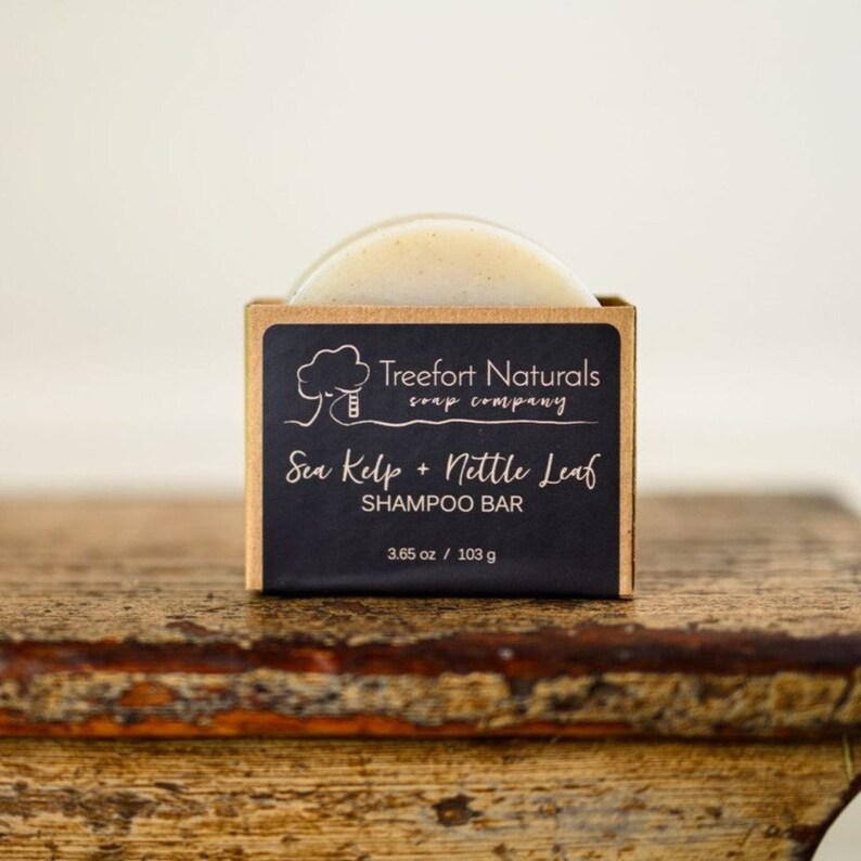 May include: A brown cardboard box with a black label that reads "Treefort Naturals soap company" and "Sea Kelp + Nettle Leaf SHAMPOO BAR" with a 3.65 oz / 103 g weight label. The box contains a round, off-white shampoo bar.