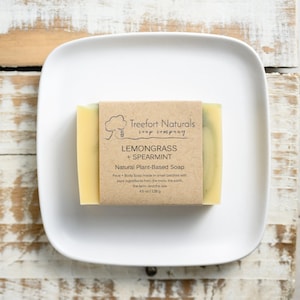 May include: A bar of natural plant-based soap with a brown paper label that reads "Treefort Naturals soap company Lemongrass + Spearmint Natural Plant-Based Soap Face + Body Soap made in small batches with pure ingredients from the trees, the earth, the farm, and the sea 4.5 oz / 128g".