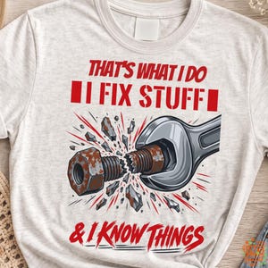 May include: A heathered light gray t-shirt featuring a graphic of a silver wrench breaking a rusty bolt and nut. The red text reads: THAT'S WHAT I DO I FIX STUFF & I KNOW THINGS. The design includes red motion lines and debris fragments.