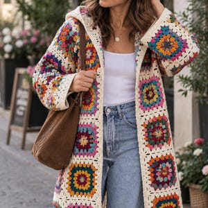 May include: A long-sleeved, hooded cardigan made of multi-colored crochet granny squares in shades of red, yellow, blue, and pink, joined by cream-colored yarn. The garment is worn over a white tank top and light blue denim jeans with a brown bag.