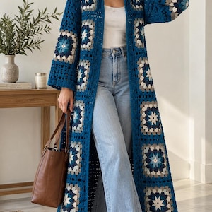May include: A long, open-front crochet cardigan featuring a repeating granny square pattern in shades of deep blue, light blue, white, and grey. The garment has long sleeves, a collared neckline, and a floor-length hem, paired with light blue jeans.